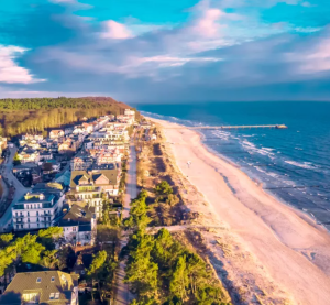 Luftaufnahme einer deutschen Ostseeinsel mit Sandstrand, Strandpromenade, Küstenwald und Häusern im Abendlicht.