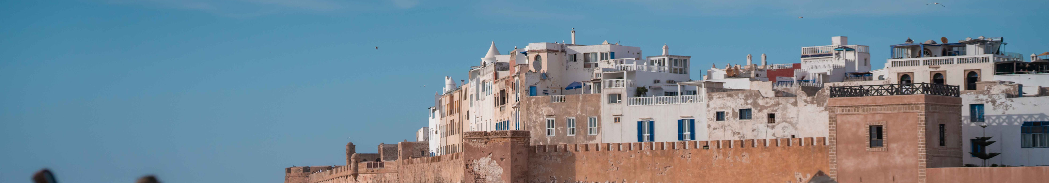 Blick auf die historische Altstadt von Essaouira in Marokko mit Stadtmauer, wei&szlig;en H&auml;usern und Fischerbooten im Vordergrund.