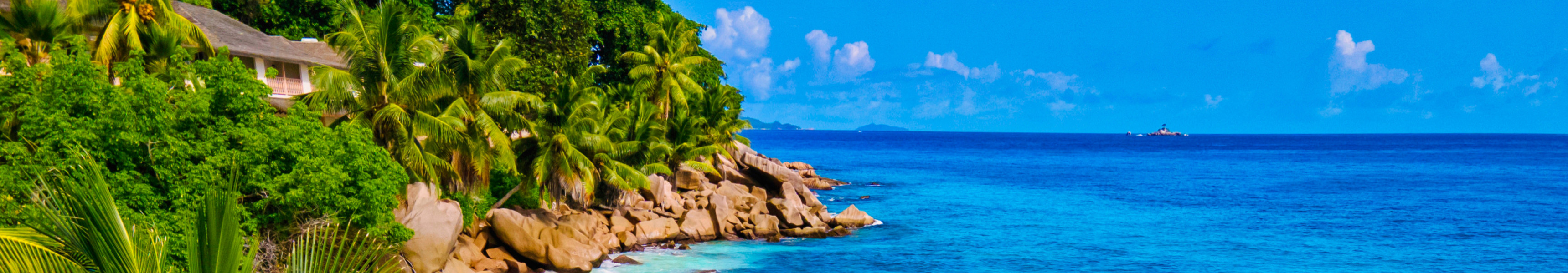 Ein Paar spaziert Hand in Hand am weißen Sandstrand von Anse Intendance auf den Seychellen, umgeben von türkisfarbenem Wasser, Palmen und beeindruckenden Granitfelsen.