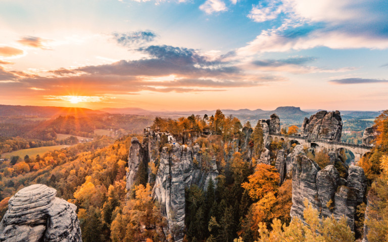 Das Naturparadies Basteibrücke im Elbsandsteingebirge, umgeben von beeindruckenden Felsen und mit einem Blick auf die herbstliche Landschaft bei Sonnenuntergang.