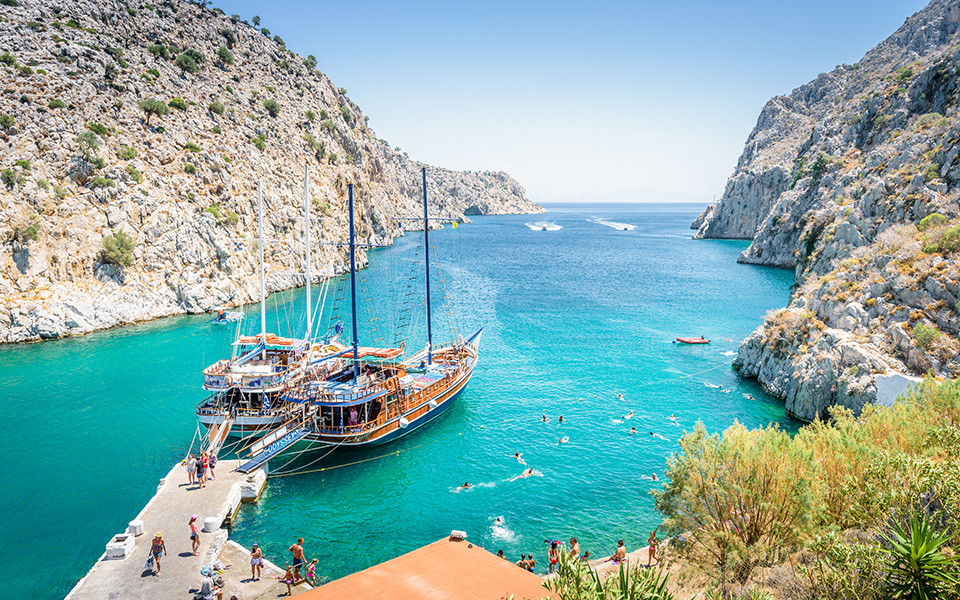 Traumhafte Bucht auf der griechischen Insel Korfu mit t&uuml;rkisblauem Wasser, steilen Felsklippen und einem traditionellen Segelboot