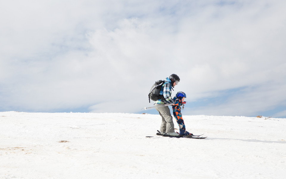 Kind und ein Erwachsener in warmen Overalls, die Skifahren üben.