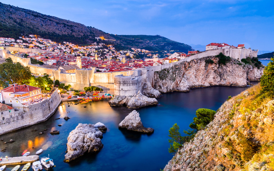 Blick auf die Altstadt von Dubrovnik mit Stadtmauer und Felsk&uuml;ste bei Abendd&auml;mmerung.